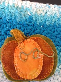 an orange is sitting on top of a crocheted blue and white blanket with a green leaf