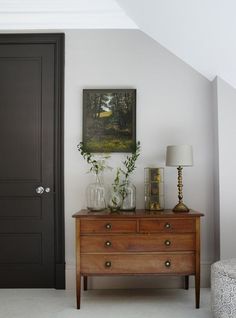 a wooden dresser sitting next to a black door in a room with a painting on the wall