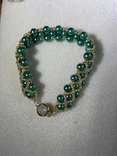 a green beaded bracelet with a gold clasp and diamond charm on it's end