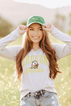 a young woman is standing in a field wearing a green hat and smiling at the camera