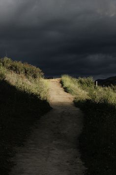 an empty dirt road leading into the dark clouds