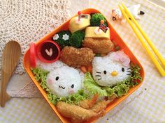 an orange tray filled with sushi and other food on top of a table next to chopsticks