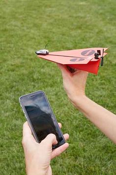 a person holding a cell phone and an origami airplane in their hand while another person holds a smart phone