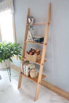 a wooden ladder shelf with books and other items on it next to a potted plant