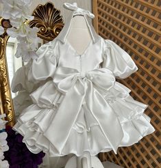 a white dress on display in front of a mirror with flowers and a gold frame