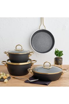 three black and gold pans on a wooden table next to a pot with a plant in it