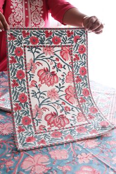 a woman is working on an intricately designed piece of cloth with red and blue flowers