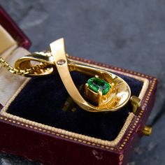 a gold ring with a green stone in it sitting on top of a velvet box