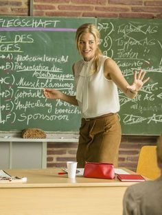 a woman standing in front of a blackboard with writing on it and holding her hands up