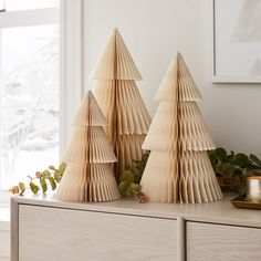 three folded paper christmas trees sitting on top of a wooden dresser next to a window