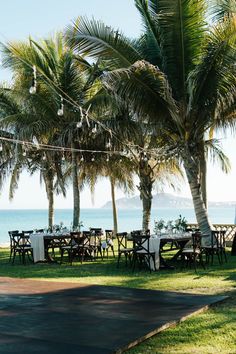 tables and chairs set up under palm trees by the ocean