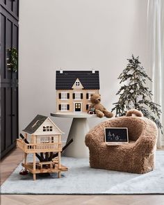 a teddy bear sitting on a chair in front of a christmas tree and doll house