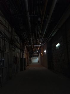 an empty dark alley with exposed pipes and light at the end is seen in this image