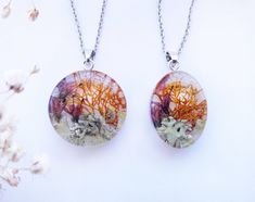 two necklaces with different designs on them sitting next to each other and flowers in the background