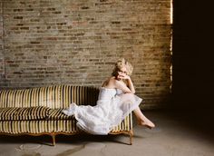 a woman sitting on top of a couch next to a brick wall