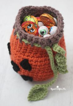 an orange crocheted bag with lots of candies in it and a green leaf