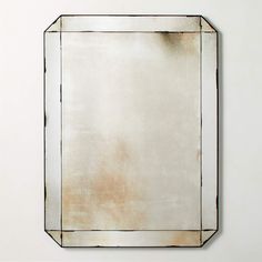 a square mirror mounted on the wall with a white back ground and light brown edges