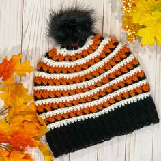 an orange and black knitted hat next to fall leaves