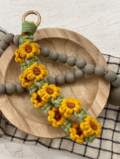 a necklace with yellow and green crocheted flowers is on a wooden plate next to gray beads