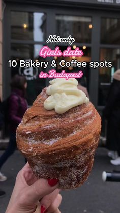 a person holding up a pastry with icing on it in front of a building