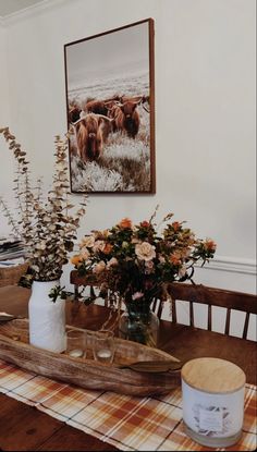 a wooden table topped with vases filled with flowers next to a painting on the wall