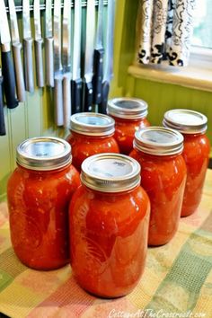 six jars of tomato sauce sitting on a table with utensils in the background