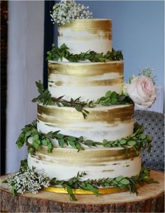 a three tiered wedding cake with greenery and flowers on the top, sitting on a tree stump