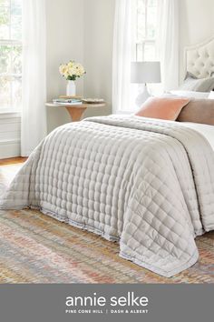 a white bed sitting next to a window in a bedroom on top of a rug