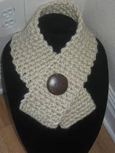 a crocheted cowl with a wooden button on the front sits on a black mannequin