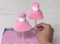 a person is holding two pink cupcakes on sticks