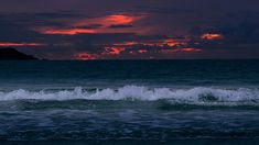 the sun is setting over the ocean with waves crashing in front of it and an island in the distance