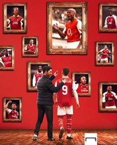 two men standing in front of a red wall with pictures on it and one man pointing at something