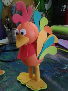 a close up of a paper sculpture of a bird on a table with paintbrushes in the background