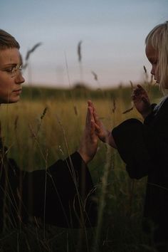 two women standing in tall grass holding hands with each other and looking at the sky