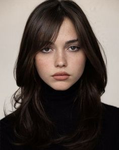 a woman with long brown hair wearing a black turtle neck sweater and dark blue eyes