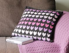 a knitted pillow sitting on top of a couch next to a book and remote control