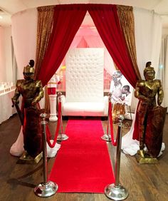 a red carpeted area with two statues on either side and a white couch in the background