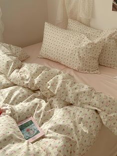 an unmade bed with white sheets and pink flowers on it, next to a window