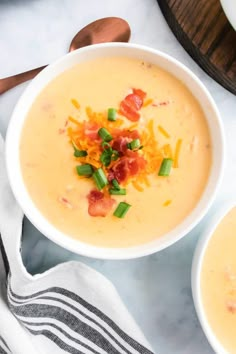 two white bowls filled with soup and topped with bacon, cheese and green onion garnish