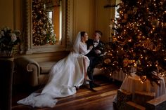 a bride and groom sitting next to a christmas tree