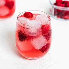 a glass filled with ice and raspberries on top of a white countertop