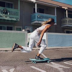 a woman riding a skateboard down the middle of a parking lot in front of an apartment building