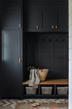 a mud room with black cabinets and baskets on the bench in front of it,