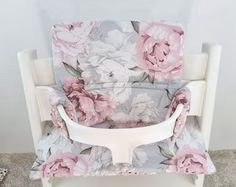 a white chair with pink flowers on the back and seat cover is sitting in front of a wall