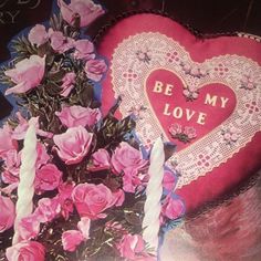 a heart shaped pillow with pink roses on it and a lit candle next to it