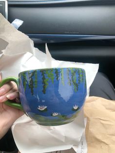 a hand holding a coffee cup with water lilies painted on the outside and inside