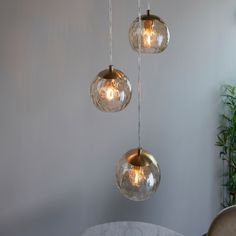 three clear glass globes hanging from a ceiling fixture in a room with a marble table and chair