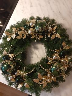 a christmas wreath with green and gold ornaments on it sitting on a counter top next to a stove