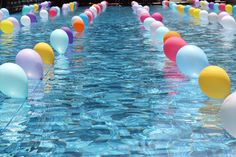 many balloons floating in the water near each other on a long line that is lined with blue, green, pink, yellow and white