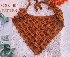 a crochet triangle is on a doily next to an orange flower